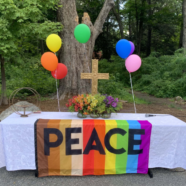 Close up of worship altar with rainbow balloons and rainbow flag that says 